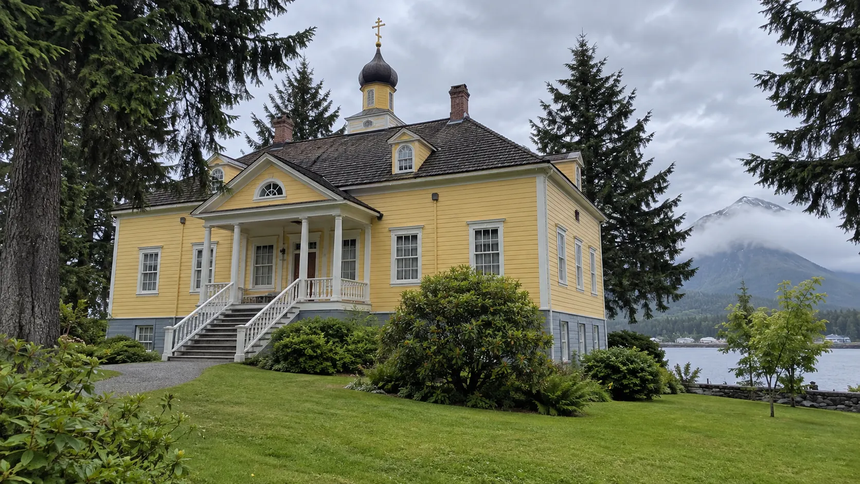 Historic Russian Bishop’s House surrounded by green lawn and spruce trees.