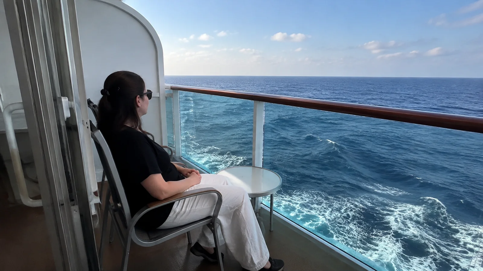 Woman relaxes on a balcony above the ship's foamy wake.