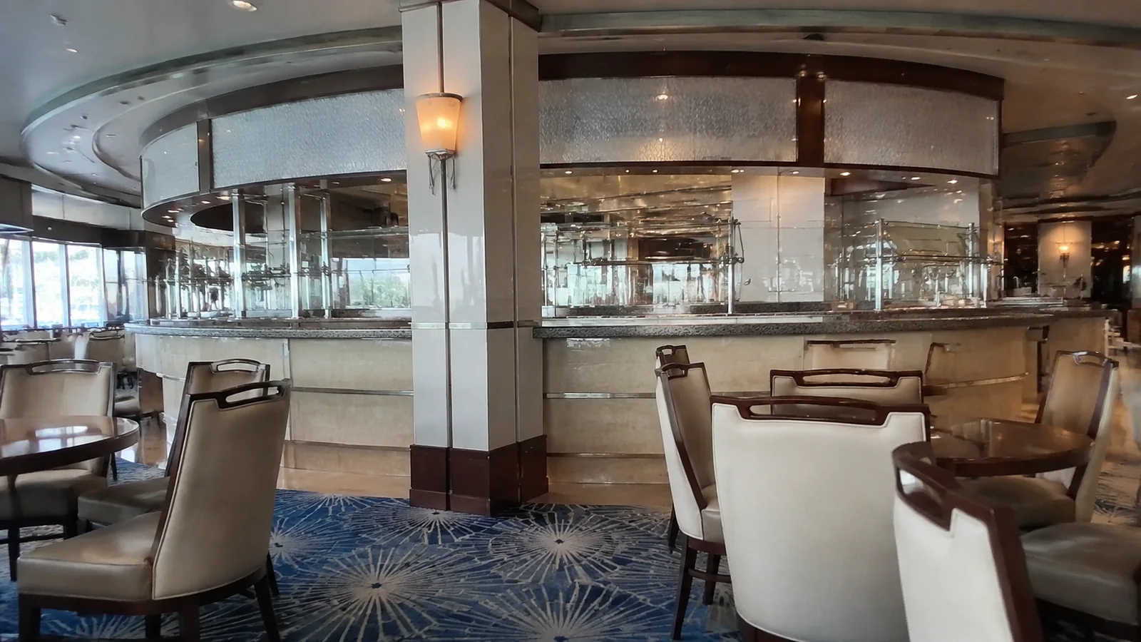 Empty lounge tables surround a curved bar on a ship.