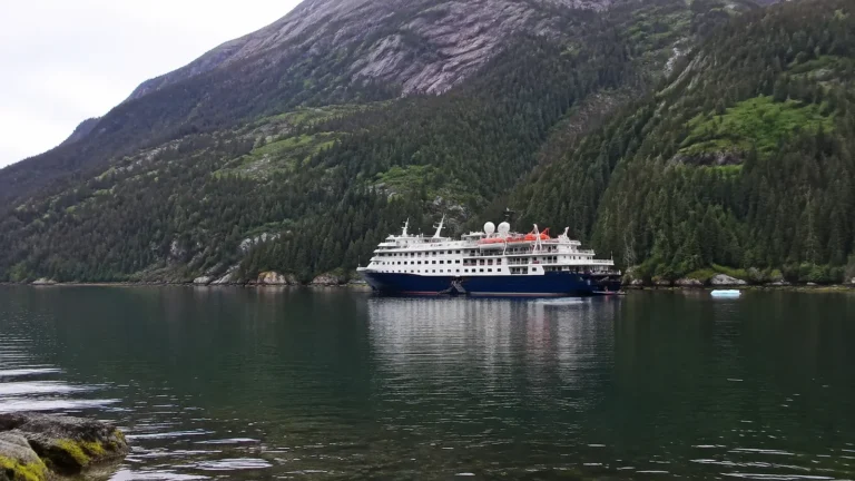 Small passenger ship beside a steep forested mountain