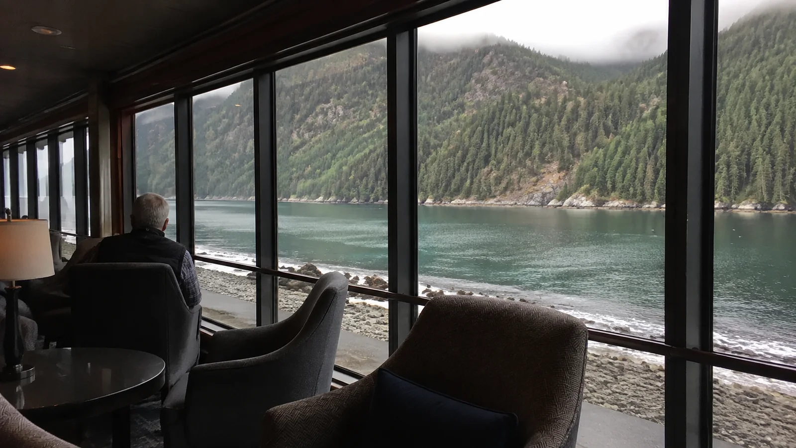 Ship's observation lounge overlooking a forested mountain shore