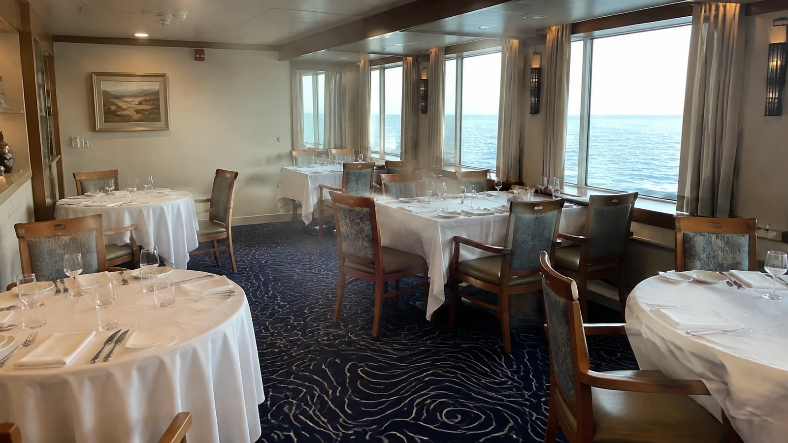 Small dining room with white tablecloths and windows overlooking the water.