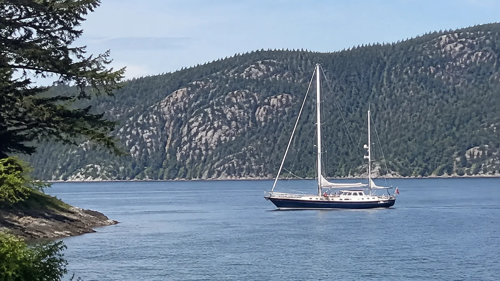 Sailboat anchored below a steep wooded mountainside.
