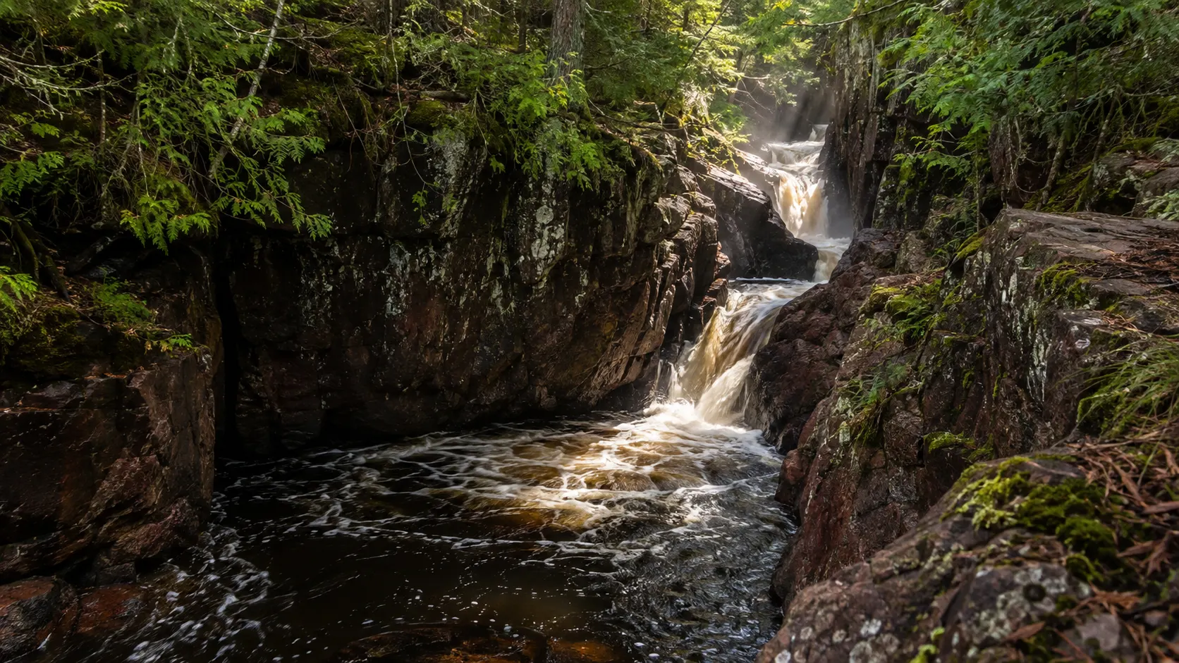 Snake Pit Falls twisting through a narrow shadowed rock channel in Amnicon Falls State Park.