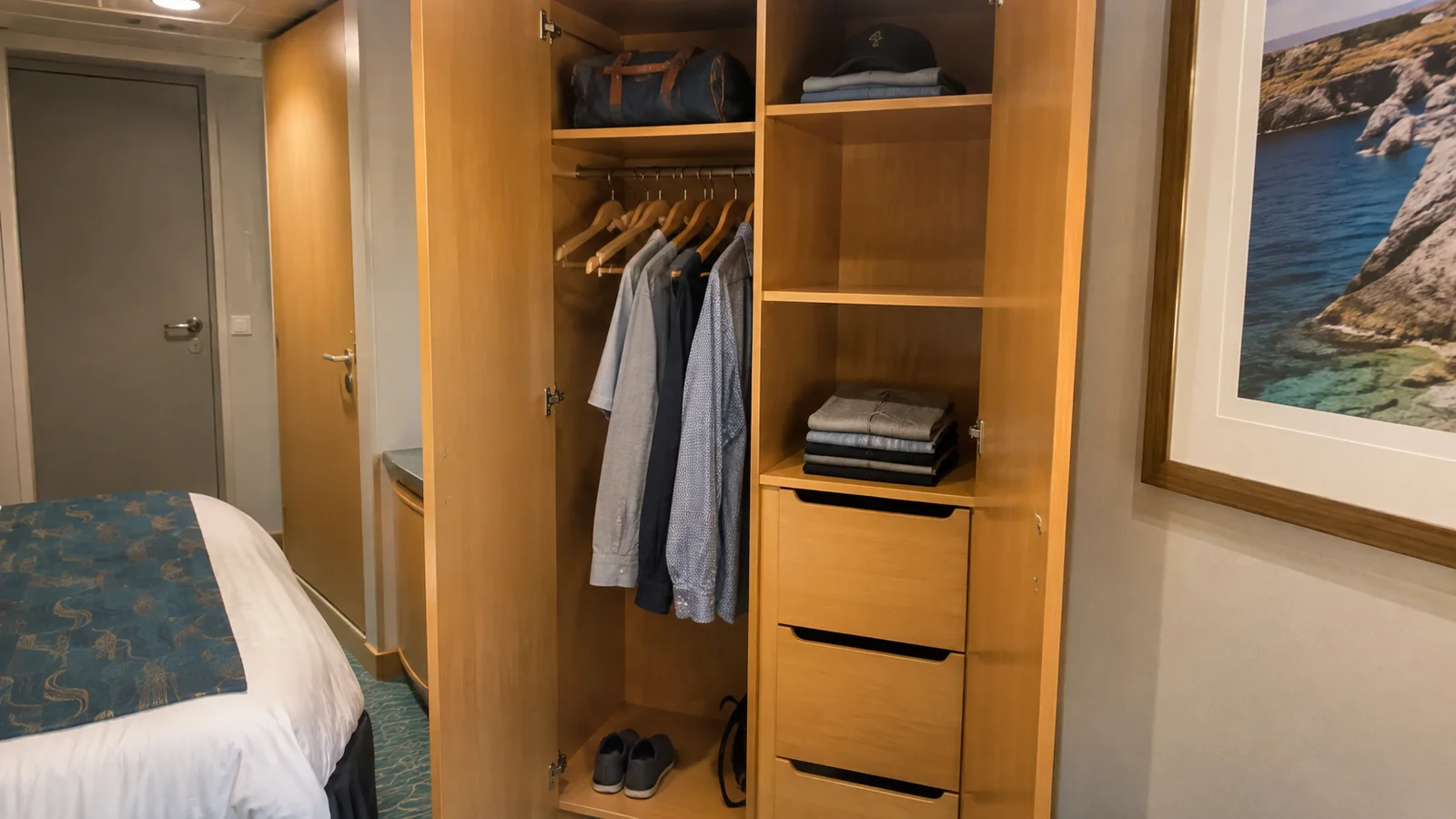 Open wardrobe holds hanging shirts and folded clothing beside a bed.