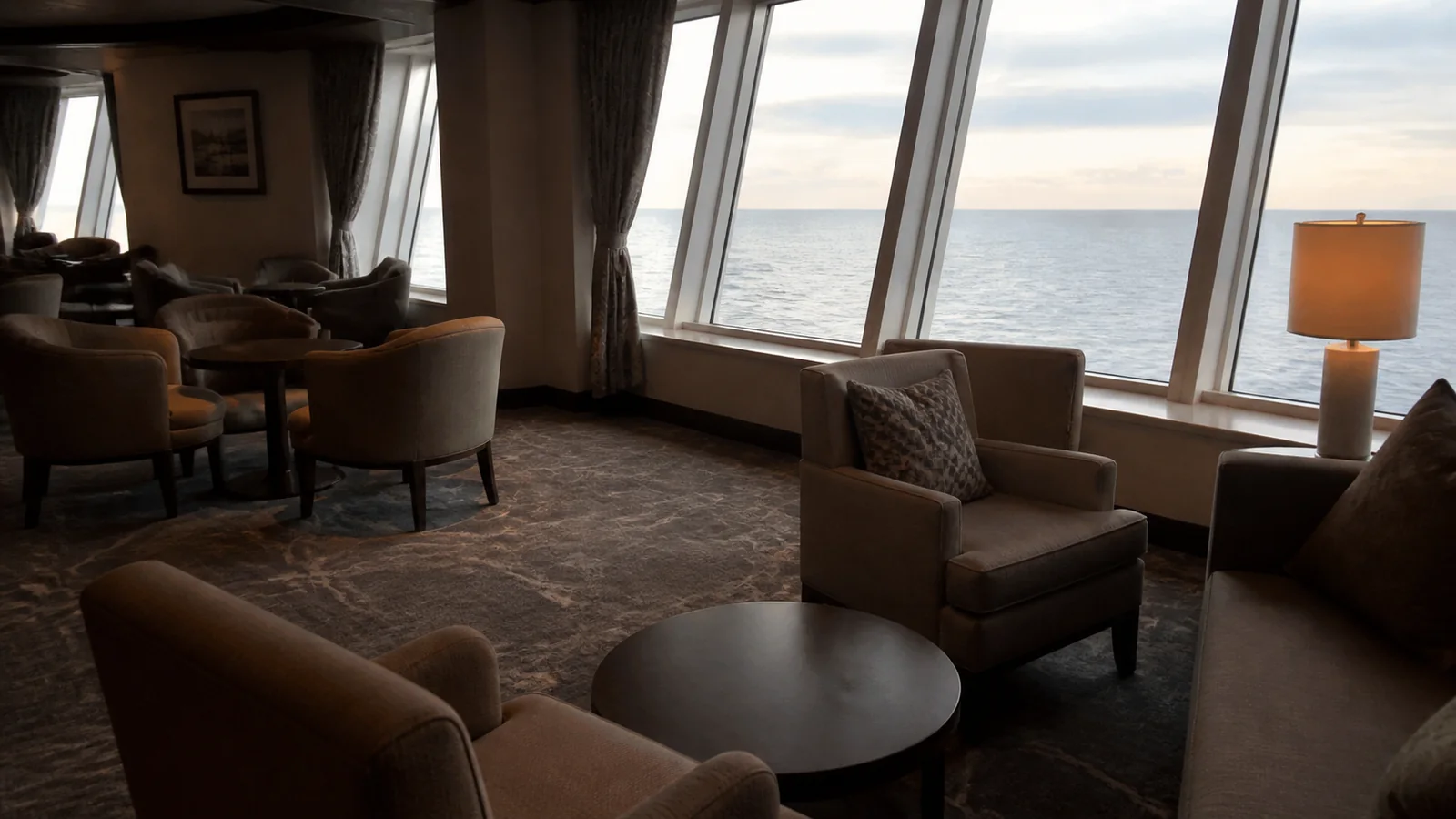 Empty ship lounge contains armchairs and large ocean windows.