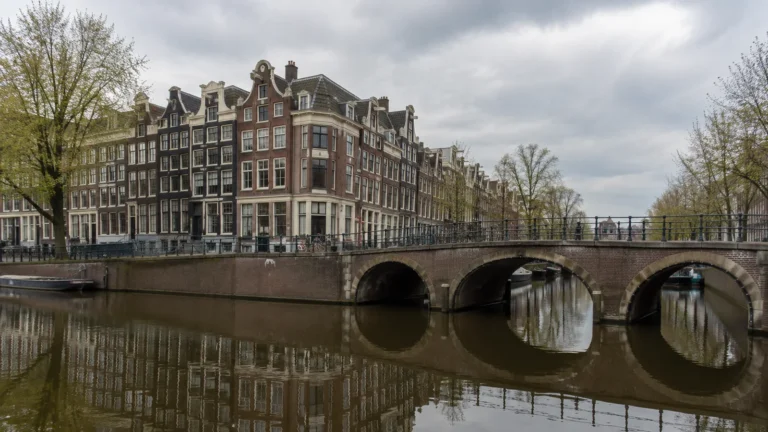 Arched bridge crosses a canal lined with tall brick townhouses.