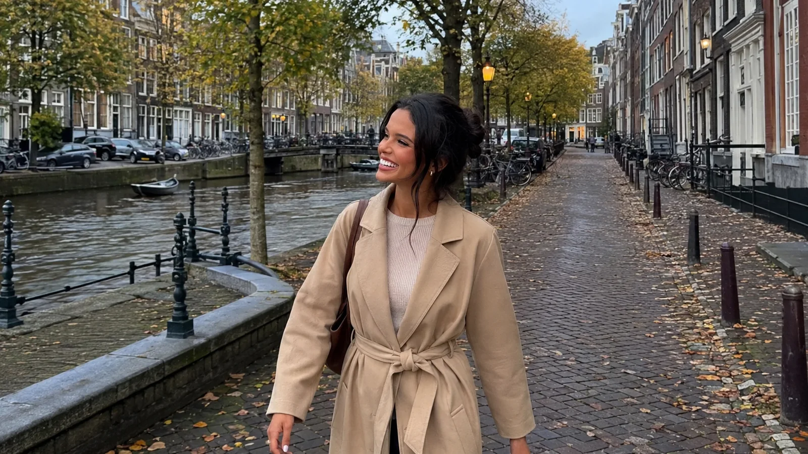 Woman walks along an autumn canal path beside historic buildings.