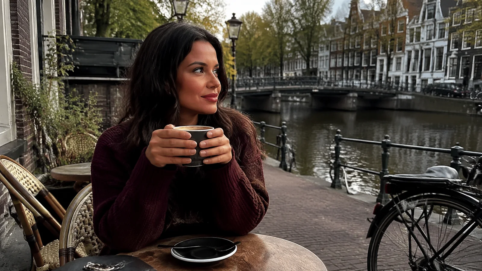 Woman holds a mug at an outdoor café beside a canal.
