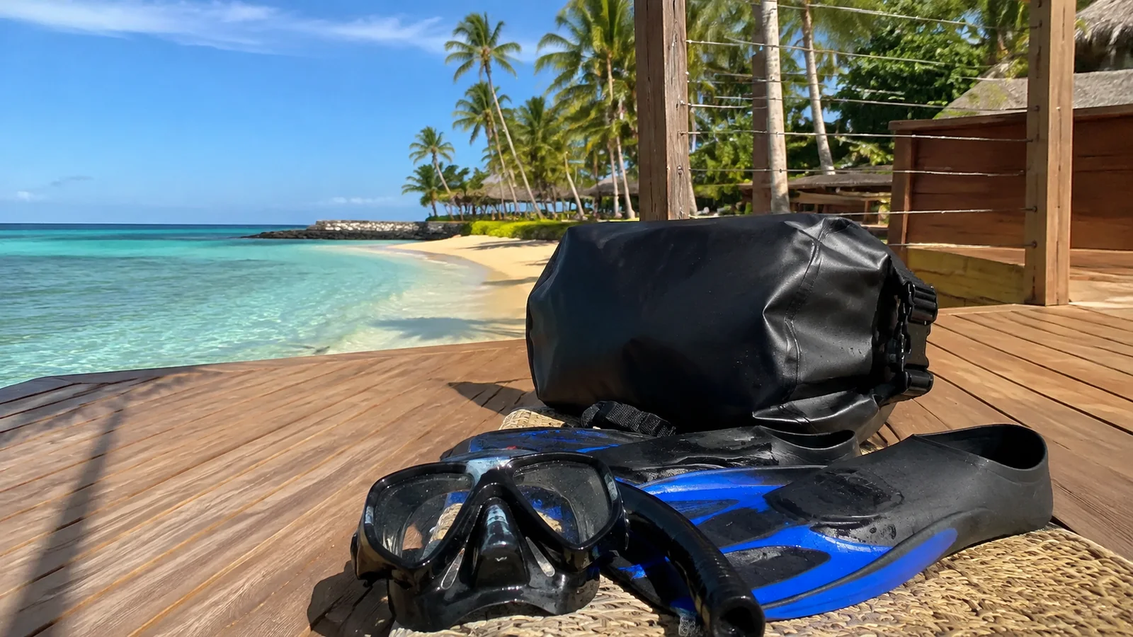 Snorkeling mask, fins, and waterproof bag rest on a seaside deck.