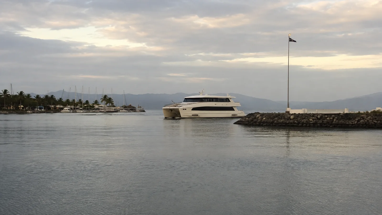 Passenger ferry passes a breakwater near a tropical shoreline.