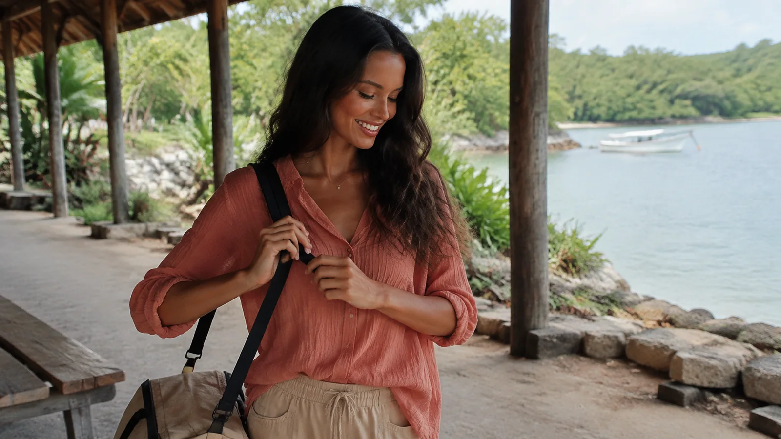 Woman adjusts her bag strap beneath a shelter overlooking a bay.