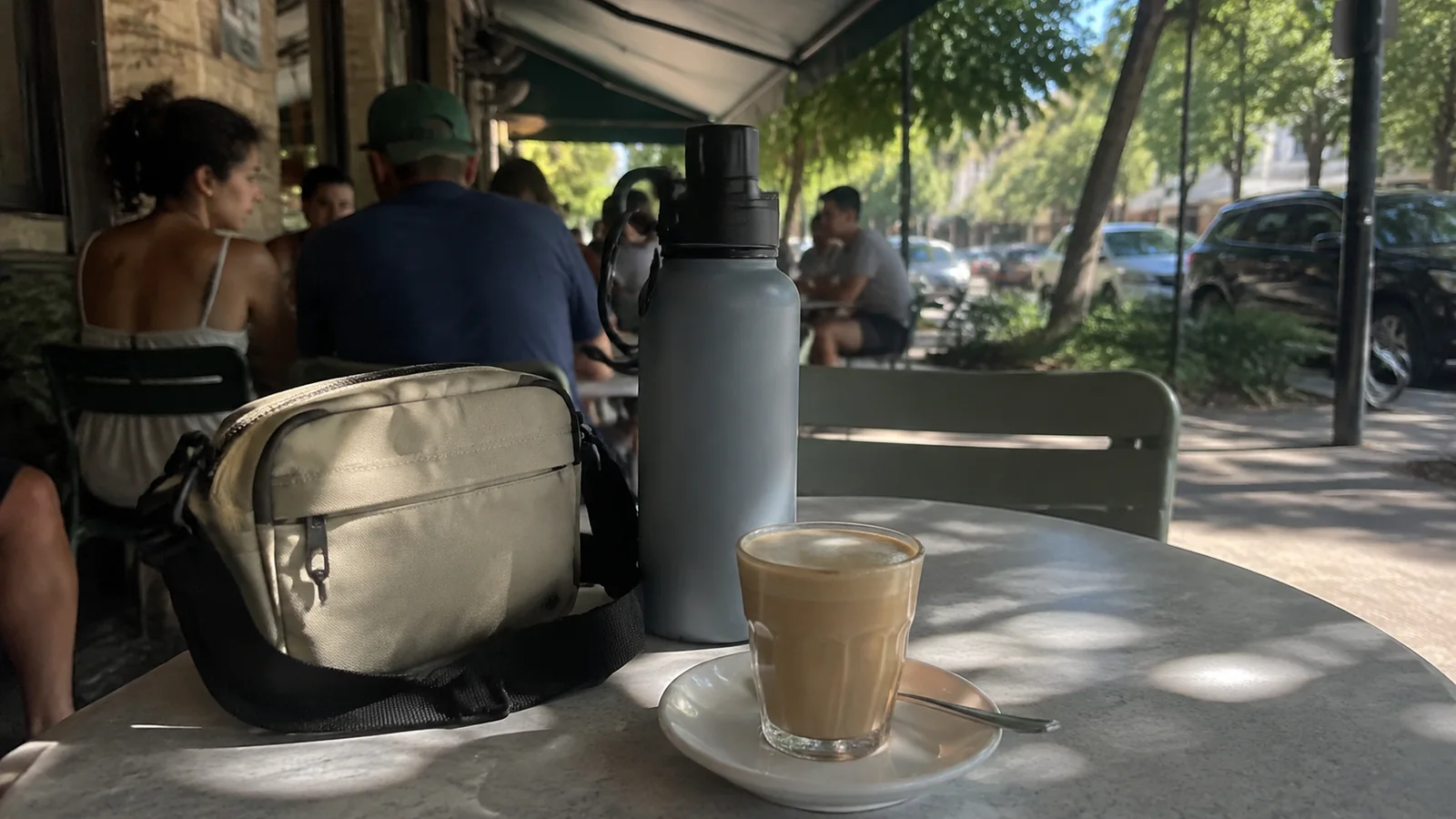 Crossbody bag, reusable bottle, and coffee glass rest on a café table.