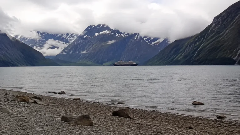 Passenger ship in a broad fjord beneath dark snow-streaked mountains.