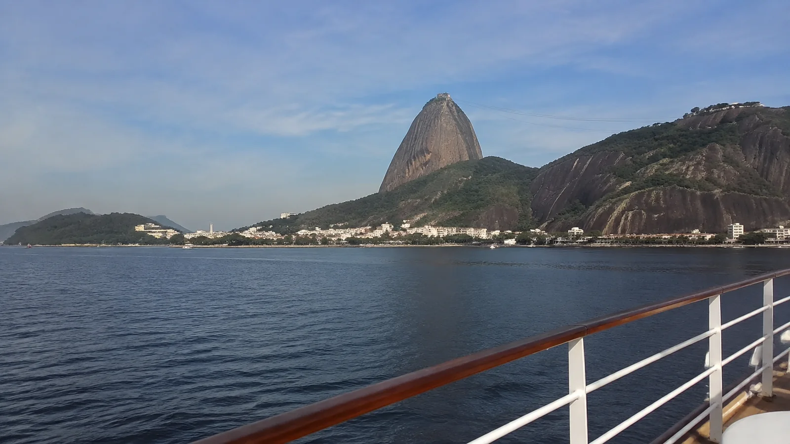 Rounded rocky peak above a coastal city viewed from ship railing.