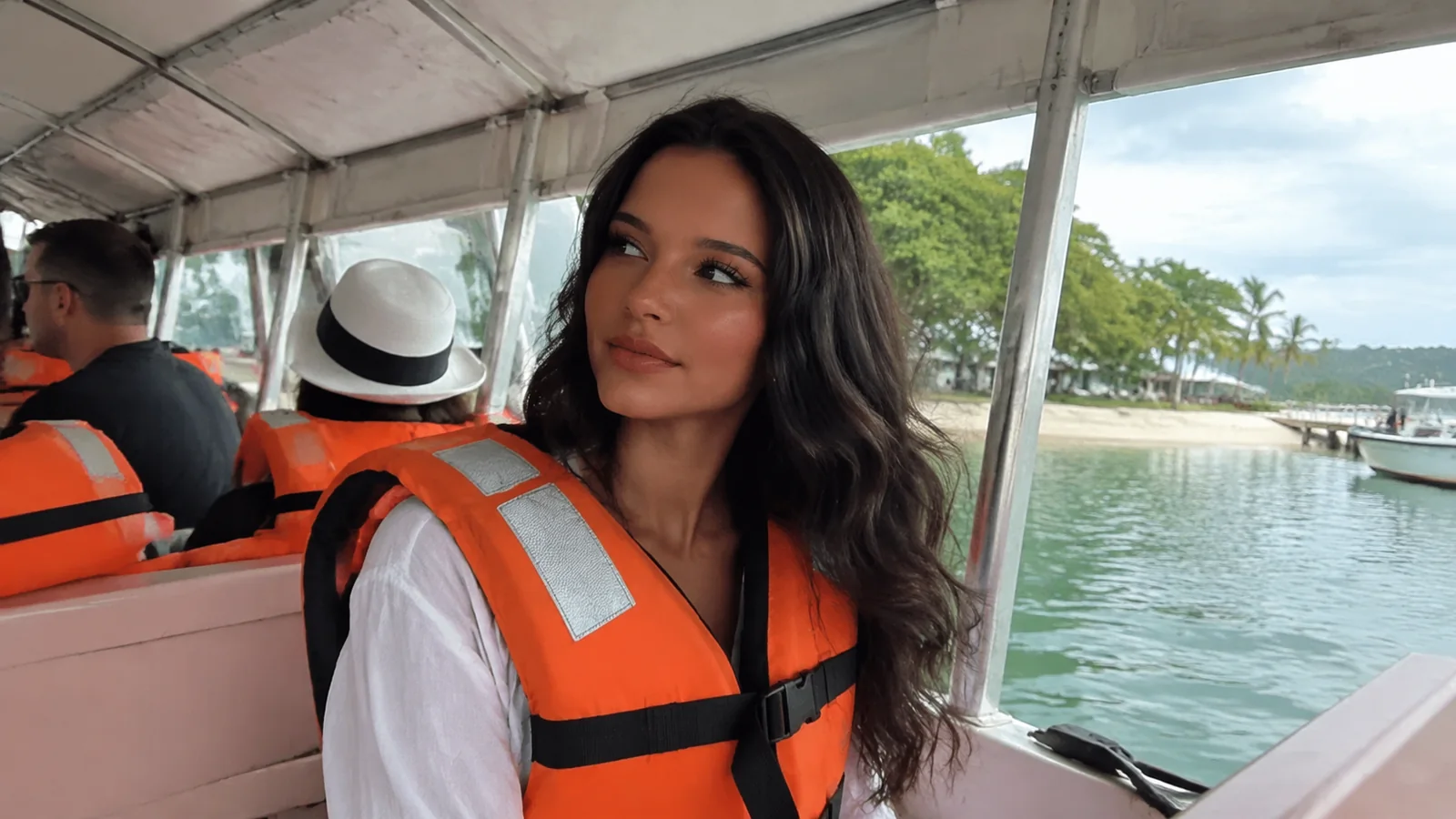 Woman wearing an orange life jacket on a covered passenger boat.