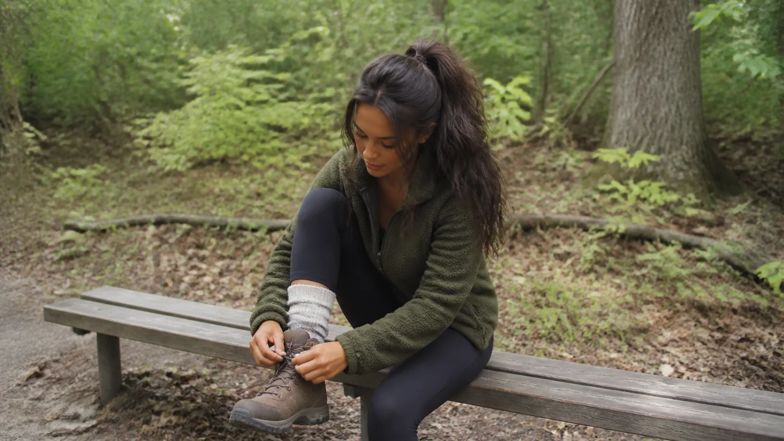 Woman tying a hiking boot on a bench in the forest.