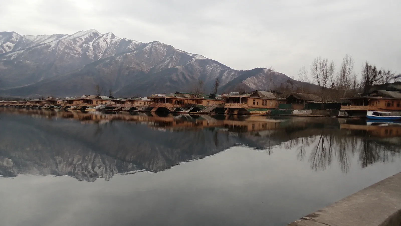 Still lake reflects snow-covered mountains and a row of houseboats.