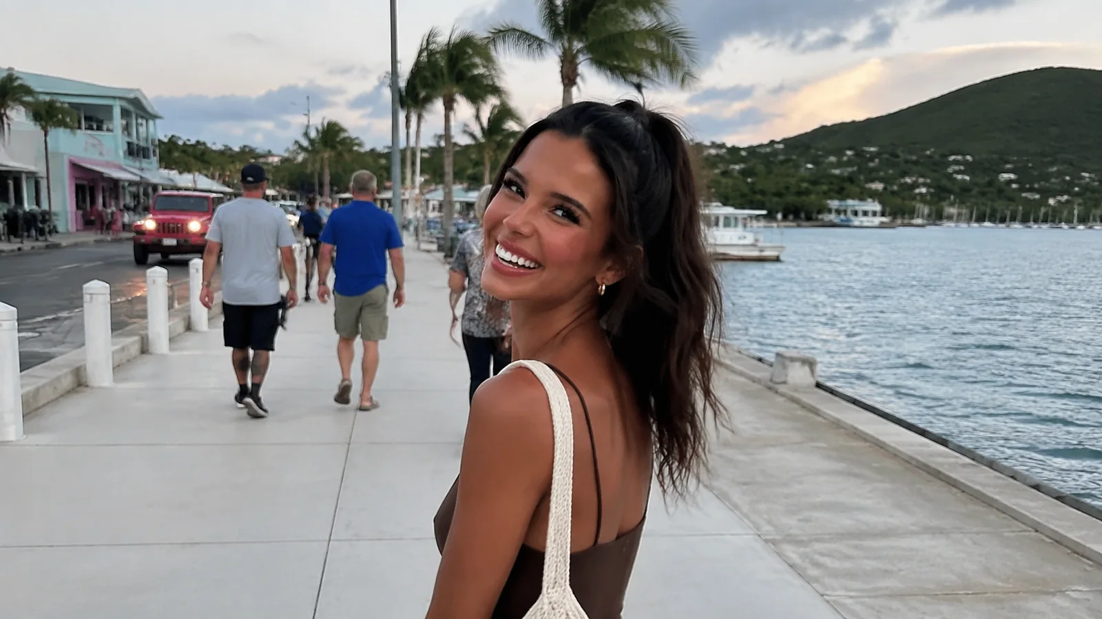 Smiling woman walking along a palm-lined waterfront promenade