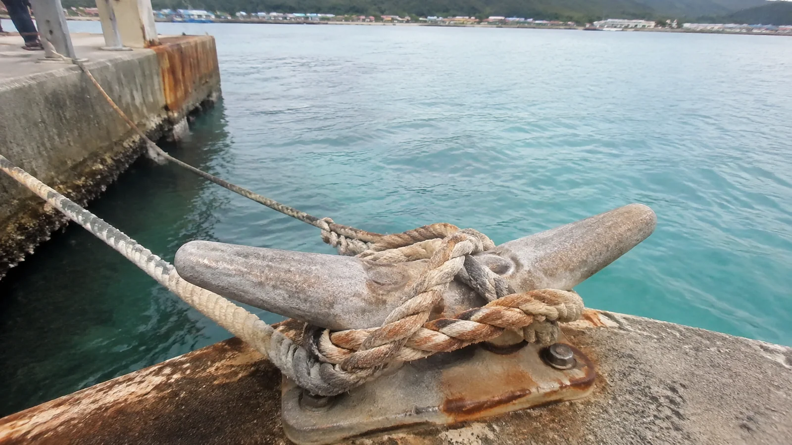 Mooring rope wrapped around a dock cleat above turquoise water