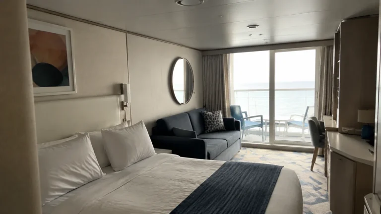 Bright balcony stateroom with a double bed, dark sofa, and ocean view.