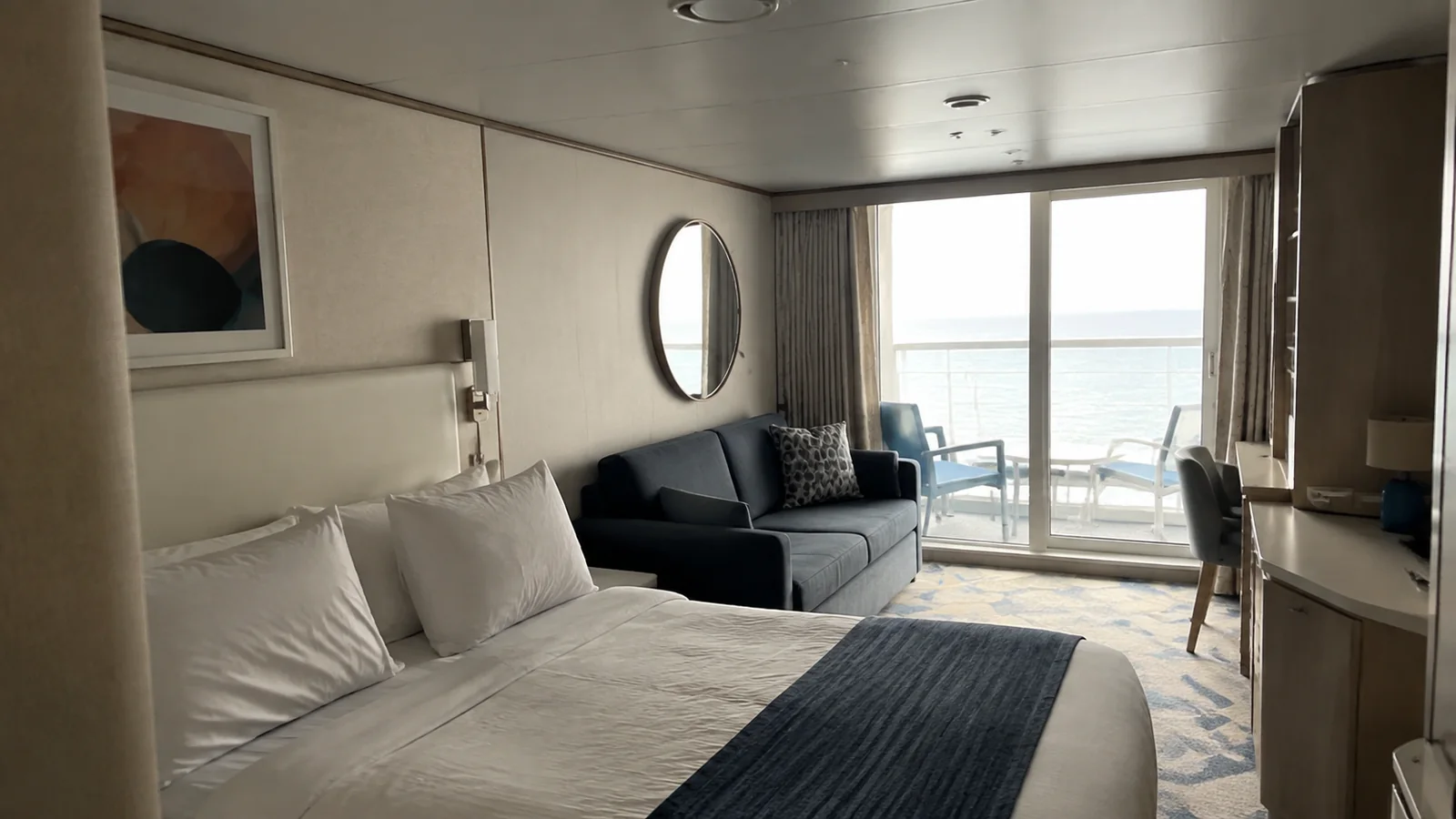 Bright balcony stateroom with a double bed, dark sofa, and ocean view.