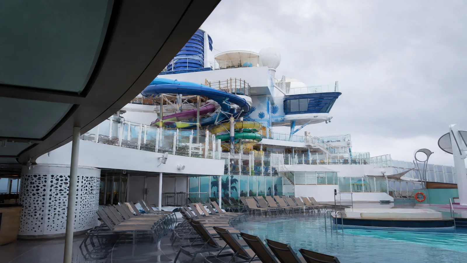 Curving waterslides rise above an outdoor cruise ship pool deck.