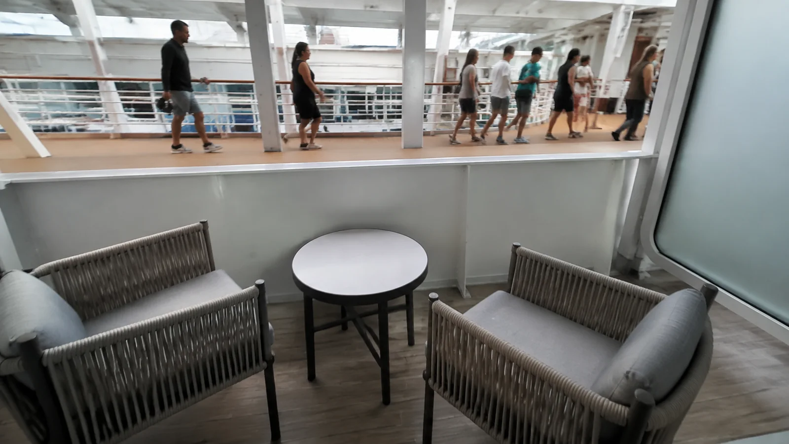 Two balcony chairs sit below a busy public ship walkway.