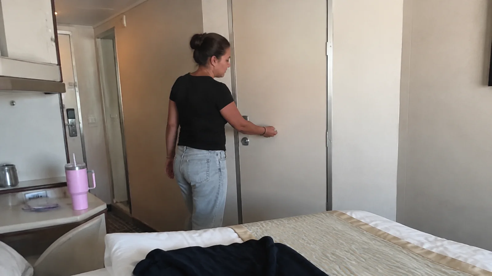 Woman opens an interior door beside a stateroom bed.