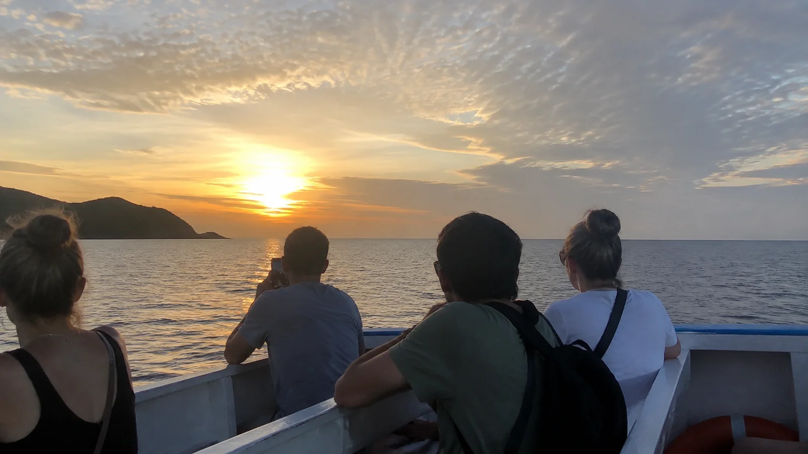 Passengers watching the sun set over the sea from a small boat.