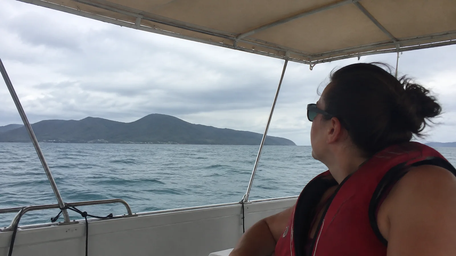 Passenger in a life jacket beneath a boat canopy near an island.