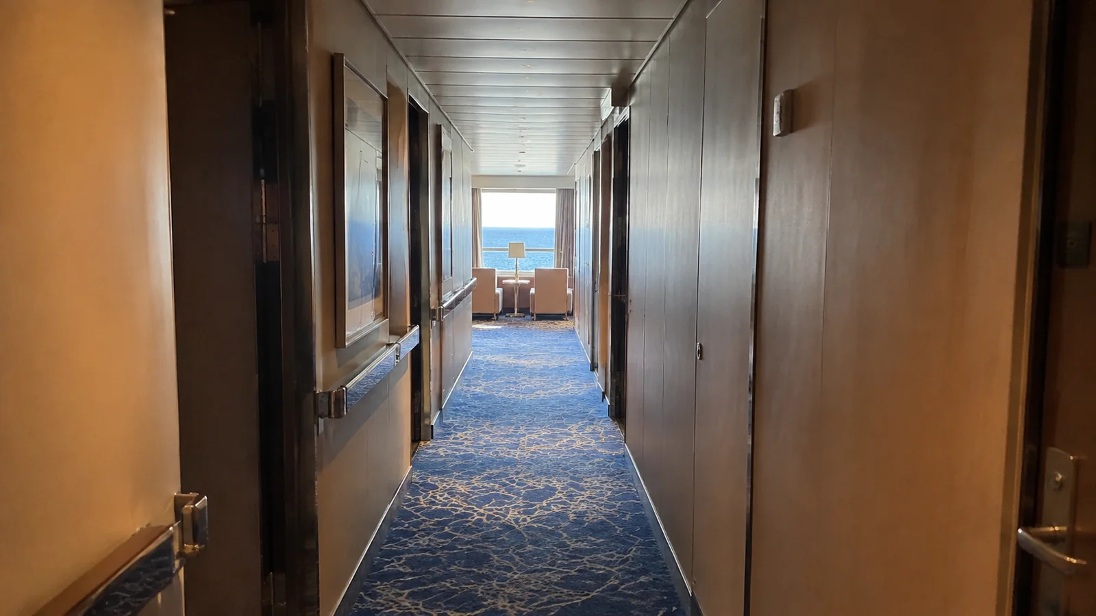 Quiet cabin corridor ending at an ocean-view seating area.