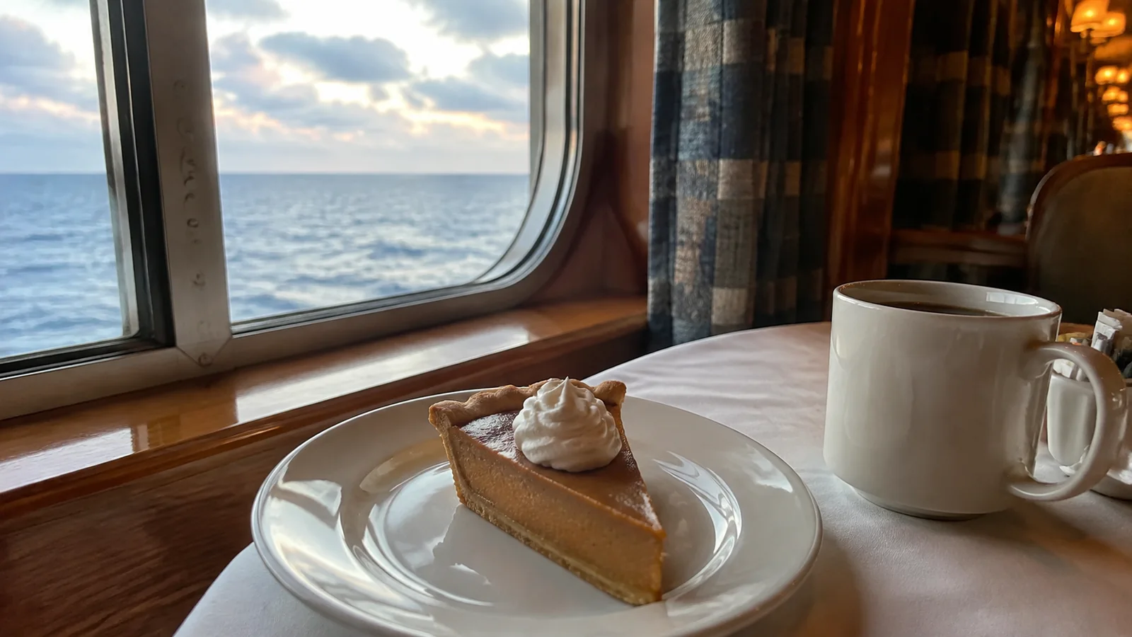 Slice of pie with whipped cream sits beside a coffee mug.