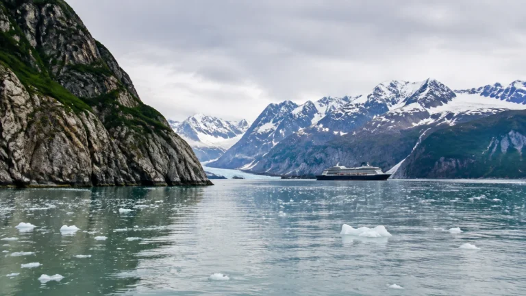 Cruise ship sailing through icy water beneath snow-covered mountains