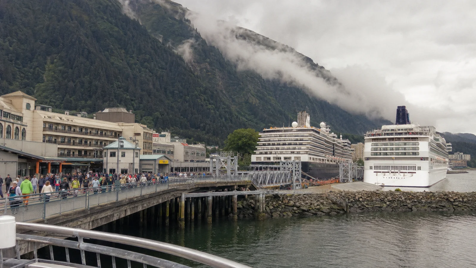 Cruise ships docked beside a waterfront town beneath misty mountains