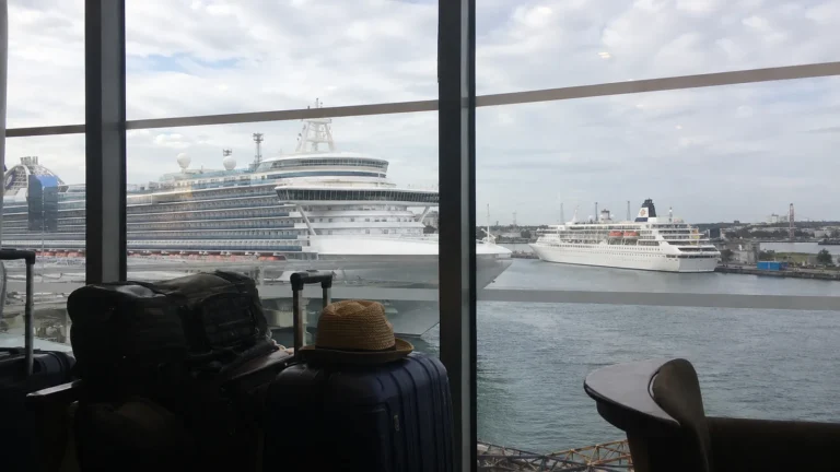 Cruise ships viewed through terminal windows beside travelers' luggage.