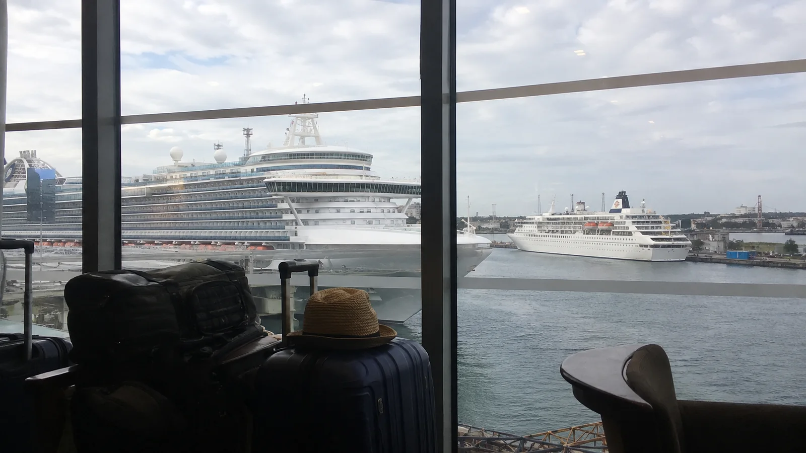 Cruise ships viewed through terminal windows beside travelers' luggage.