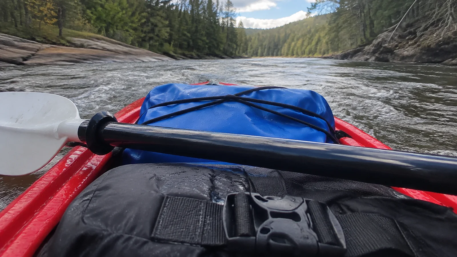 Paddle and secured dry bags on the bow of a kayak traveling down a river