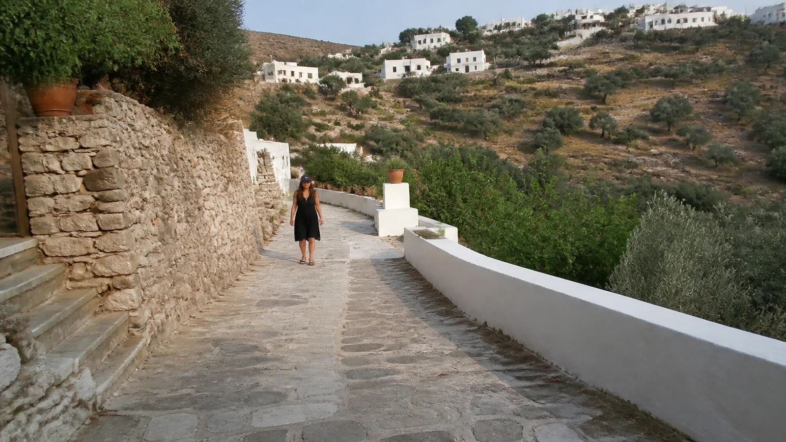 Stone-paved path winding between white walls and a terraced hillside.