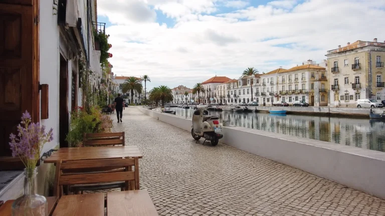 Waterfront promenade with outdoor tables beside a canal and rows of white historic buildings