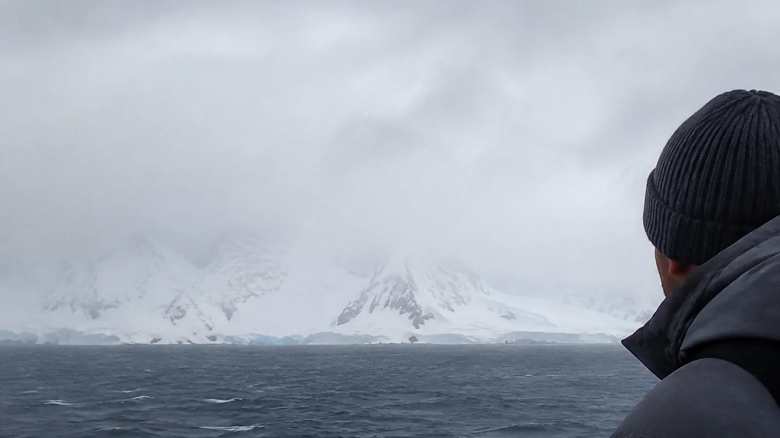 Passenger viewing a snow-covered coast through mist and rough weather.