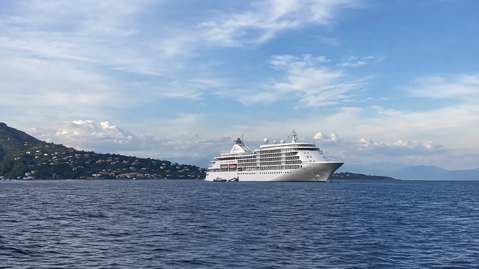 White cruise ship sailing near a hilly coastline