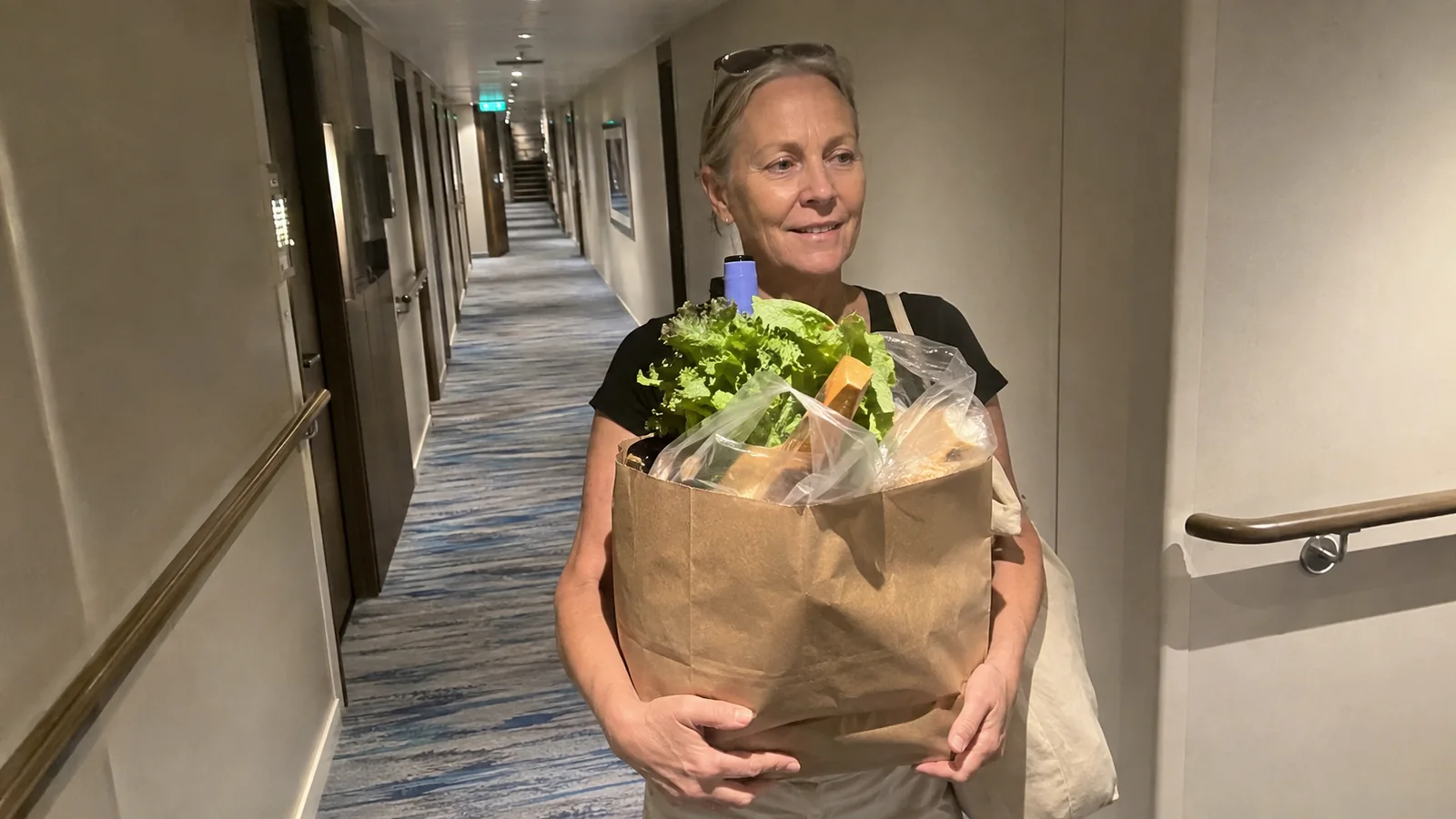 Woman carrying a paper bag of groceries through a ship's corridor