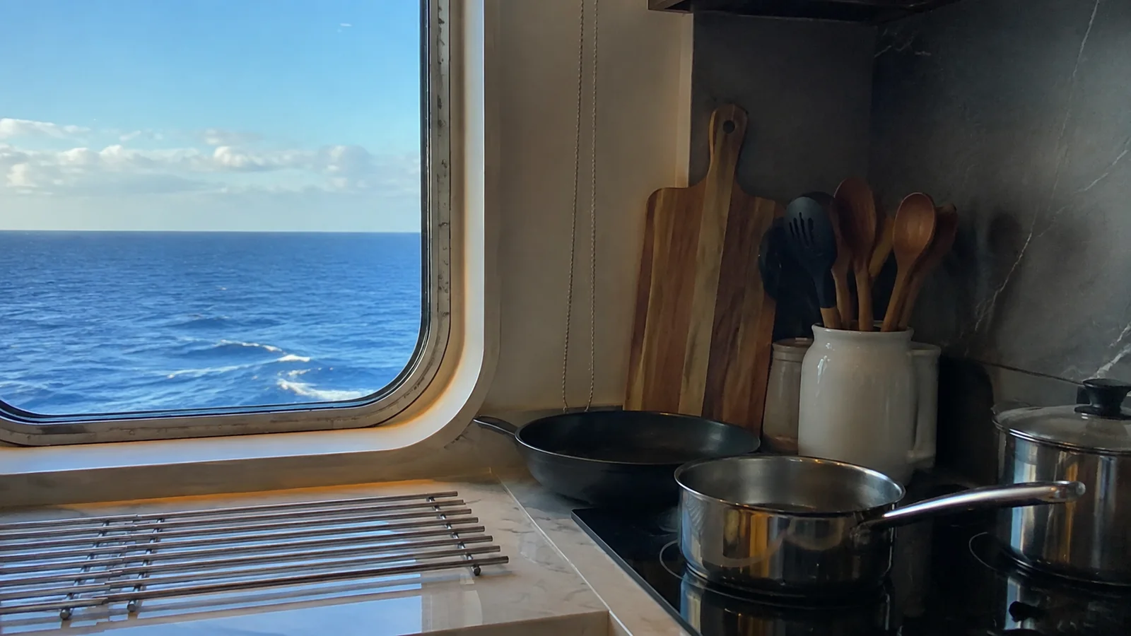 Cookware and utensils in a ship's kitchenette beside an ocean-view window