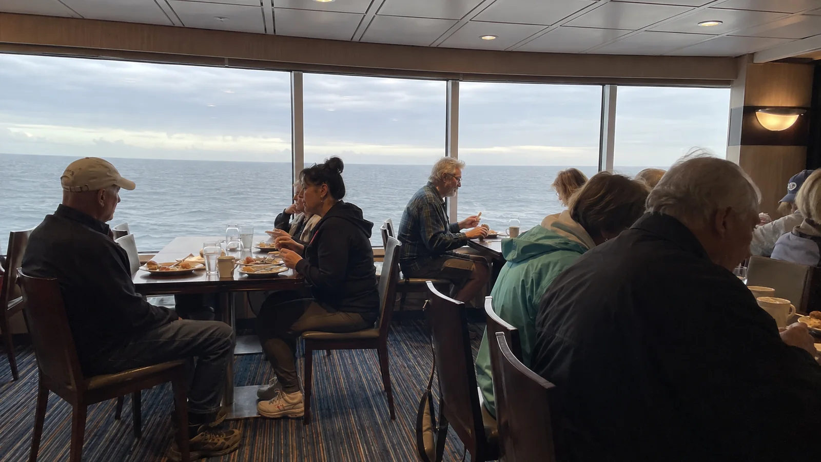 Passengers dining beside broad ocean-view windows.