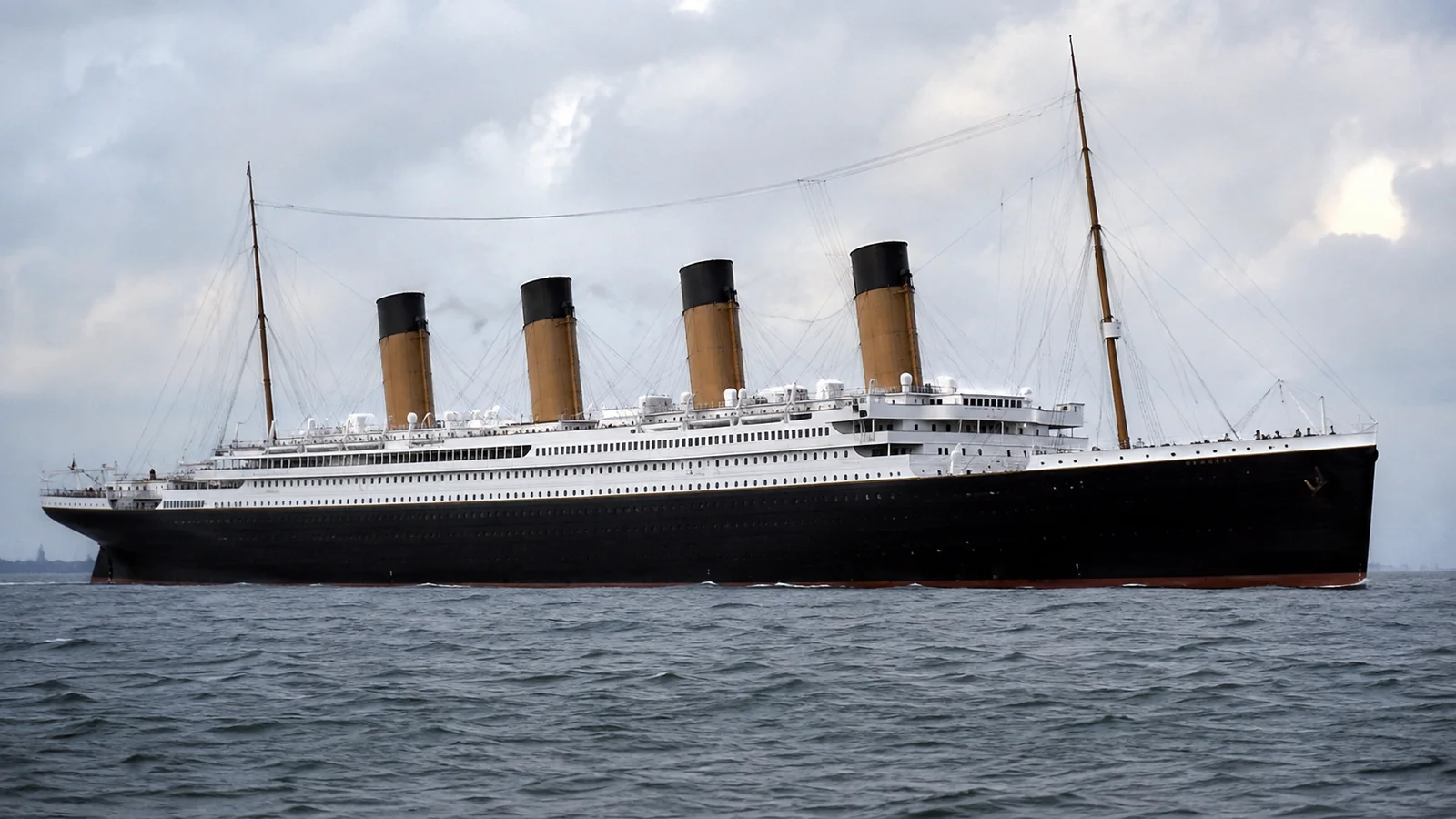 Black-hulled ocean liner with four yellow funnels on gray water.
