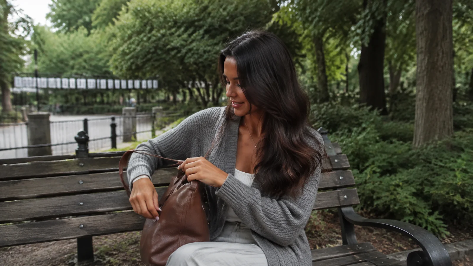 Woman packing a brown bag on a bench beside a wooded waterway.