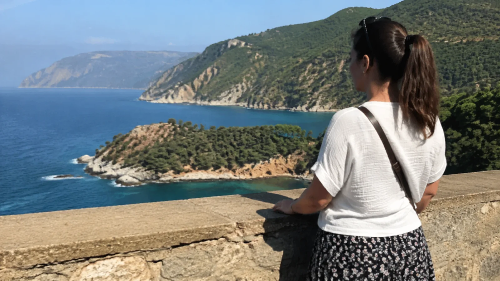 Woman looks across a blue bay from a stone overlook.