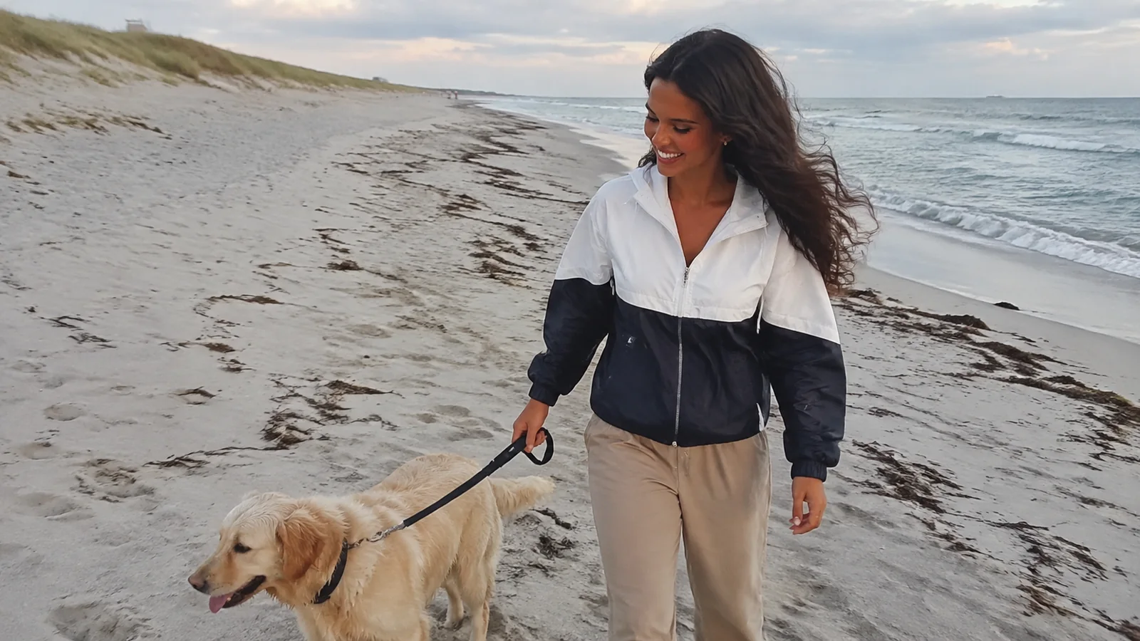 Woman walking a leashed golden retriever along a sandy beach.