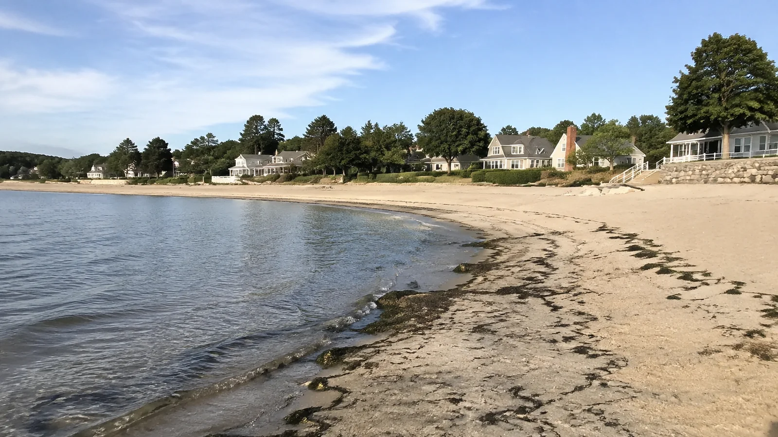 Quiet sandy beach curving past waterfront homes.